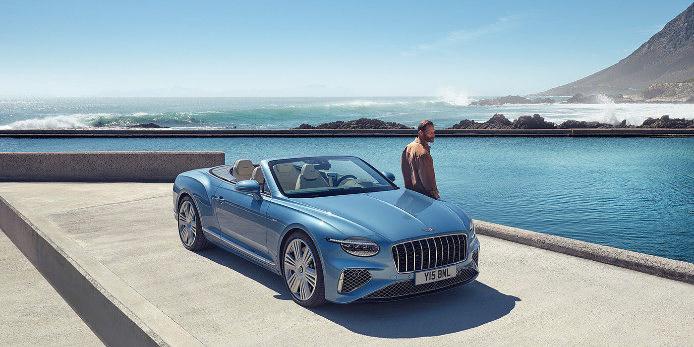 Bentley Macau New Bentley Continental GTC Azure convertible front view in Light Windsor blue paint with 22 inch ten spoke wheels parked by the sea in the sunshine