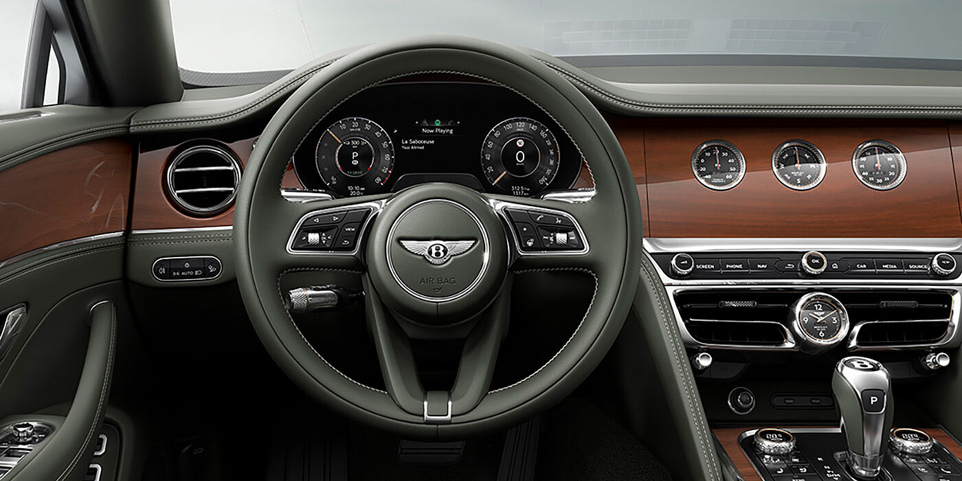 Bentley Macau New Bentley Flying Spur sedan front cabin in Cumbrian Green hide and Crown Cut walnut veneer showing steering wheel and Rotating Display with three clocks on face