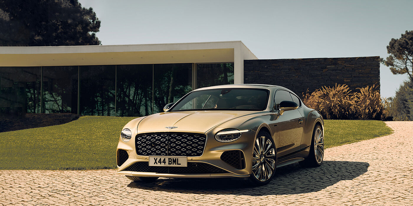 Bentley Macau Bentley Continental GT Mulliner coupe front three quarters in Patina paint parked outside a glass fronted building with a grass lawn behind it